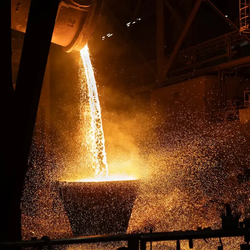 Molten steel pouring in a bright, glowing stream from an industrial ladle into a container, throwing sparks throughout the North Star BlueScope Steel facility.